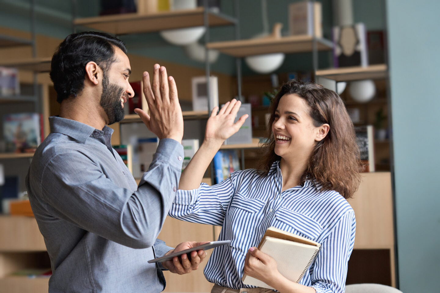 Two happy friendly professionals giving high five standing in office.