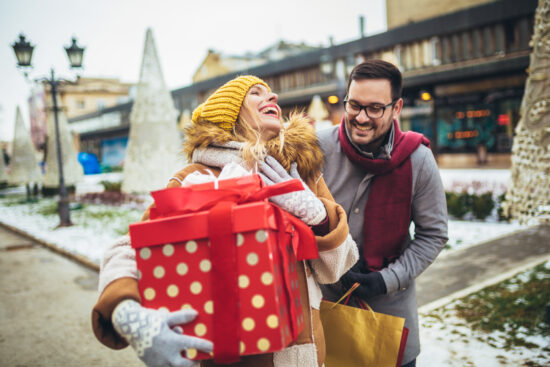 Young couple dressed in winter clothing holding festive gift boxes outdoor