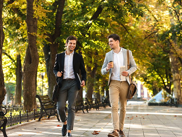 male workers walking through the park and smiling with a coffee