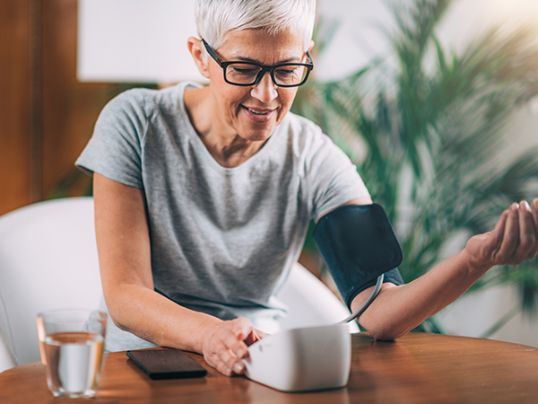 short haired woman wearing glasses and checking blood pressure reading