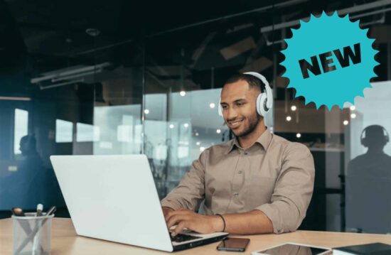 Smiling man with headphones on sat at a desk looking at a laptop