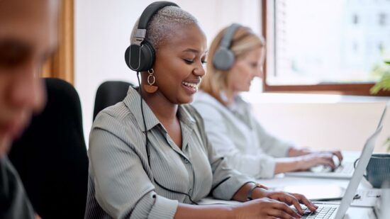 Female employees with headphones on typing on laptops