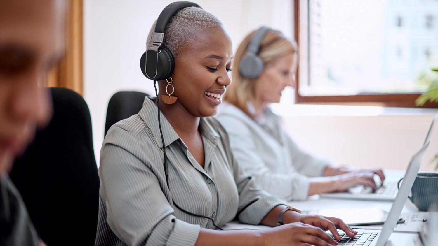 Female employees with headphones on typing on laptops