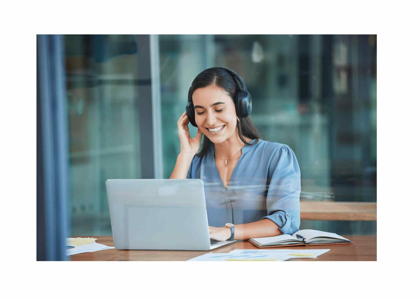 Smiling female employee sat in a quiet office setting in front of a laptop with headphones on.