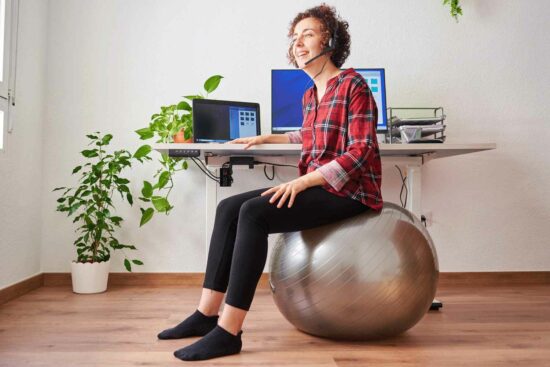 Remote worker sat at desk facing away from laptop, sitting on an exercise ball.