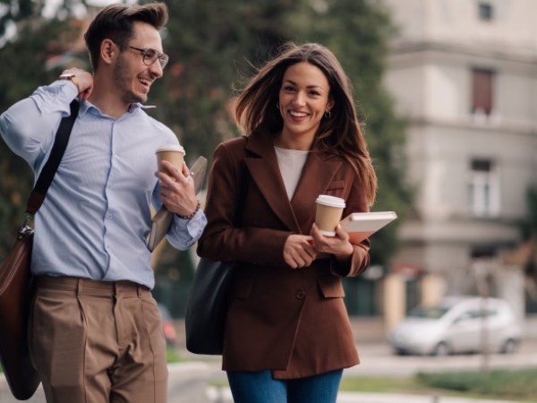 Man and woman talking holding coffee and office supplies whilst talking outside