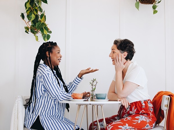 Two females sat opposite one another at a small table having a conversation over coffee