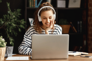Female wearing headphones sitting in front of laptop, smiling