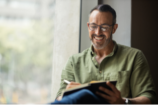 mProve in 30 January cover image shows man wearing glasses sat by the window smiling as he writes in a notebook